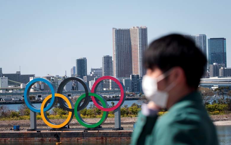 Un hombre con una mascarilla, en medio de las preocupaciones por la propagación del nuevo coronavirus COVID-19, se encuentra frente a los anillos olímpicos desde un punto de observación en el distrito de Odaiba de Tokio el 25 de marzo de 2020, el día después de la histórica decisión de posponer el Tokio 2020.