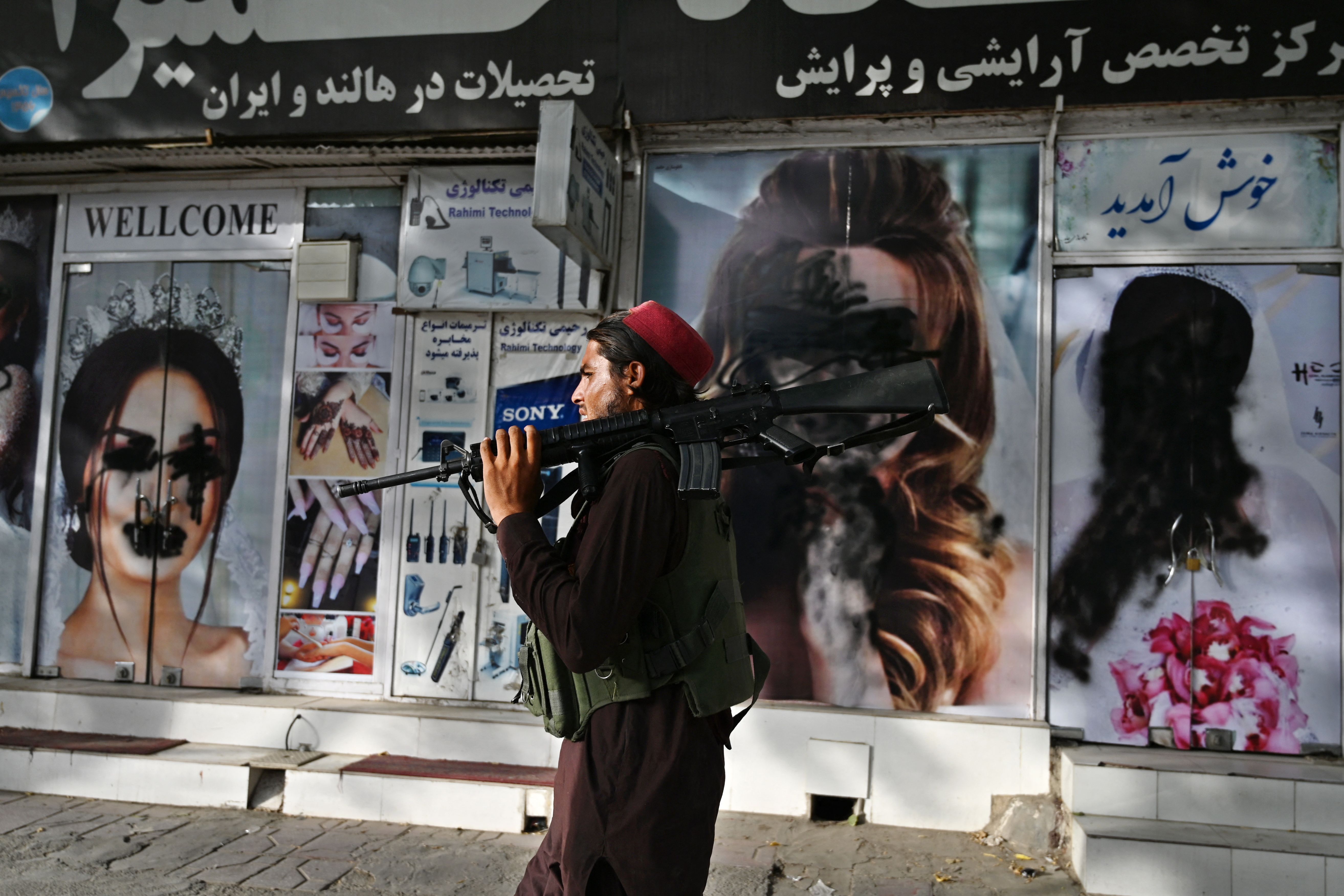 Un combatiente talib&aacute;n pasa frente a un sal&oacute;n de belleza con im&aacute;genes de mujeres desfiguradas con pintura en aerosol en Shar-e-Naw en Kabul el 18 de agosto de 2021